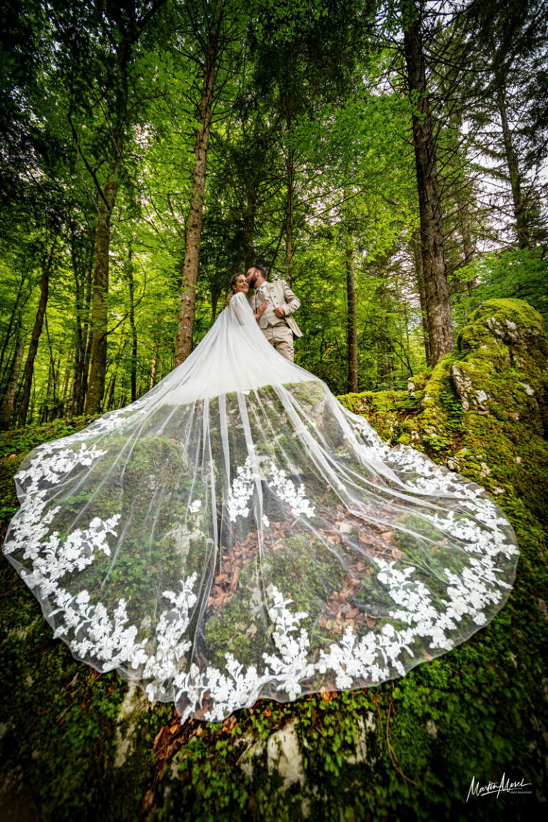 Des mariés enlacés avec un magnifique voile au premier plan, le tout en forêt