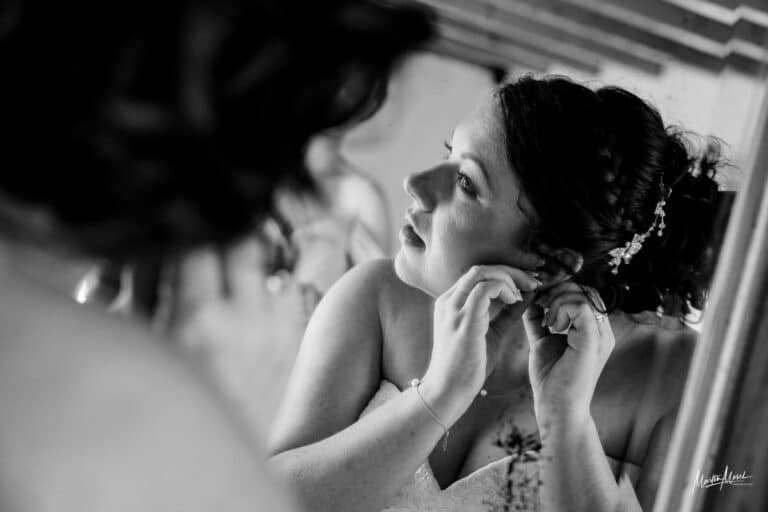 La mariée accroche ses boucles d'oreilles face au miroir
